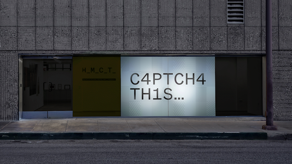 An exterior shot of the HMCT building with a projected, animated piece displaying the CAPTCHA THIS logo on a background made of analphabetic characters